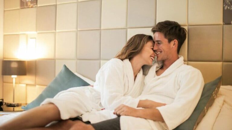 Affectionate young couple wearing bathrobes hugging on comfortable bed in modern apartment while resting together